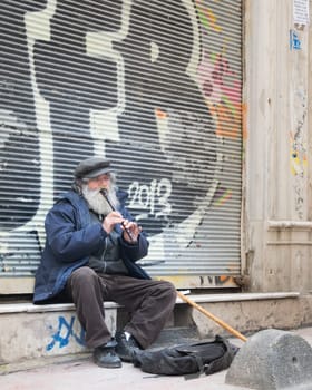 Istanbul, Turkey - April 24, 2017: Old street musician playing treble recorder instrument for money in front of grunge metal rolling door with graffiti of abandoned shop at Istiklal street