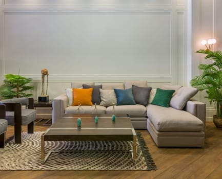 Comfortable gray sofa with colorful cushions placed near table on rug in spacious modern room with armchairs and green potted plants