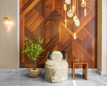 Modern white feather armless chair, squared coffee table, and short wooden planter with green bushes, in a hall with decorated wood cladding wall, and white marble floor