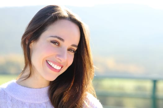 Happy woman with perfect smile looks at camera outside a sunny day