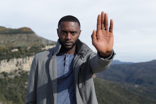 Front view portrait of an angry man with black skin gesturing stop in winter in nature