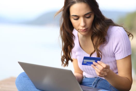 Serious woman buying online using laptop and credit card in nature