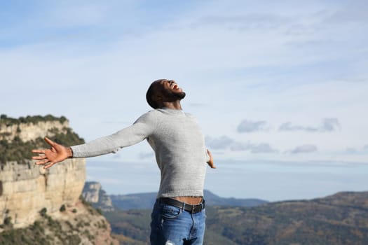 Excited man with black skin celebrating vacation in the mountain outstretching arms