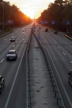 Moving cars on the motorway at sunset time. Highway traffic at sunset with cars. Busy traffic on the freeway, road top view