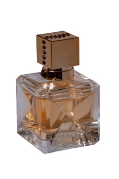 Perfume products isolated. Closeup of a gold brown glowing perfume glass bottle isolated on a white background. Empty label. Eau de Parfum. Clipping path. Macro photograph.