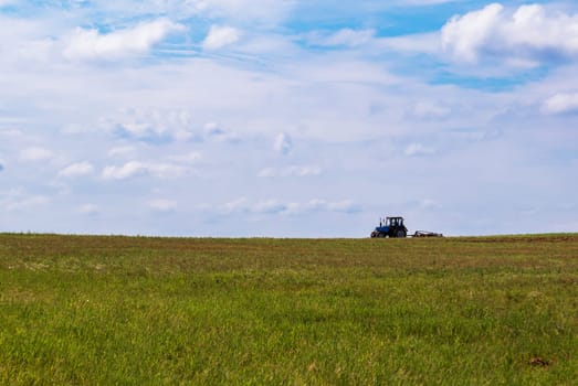 Tractor working in the field, plowing the land, preparing for sowing. View of the field and tractor in the distance against a blue sky with clouds