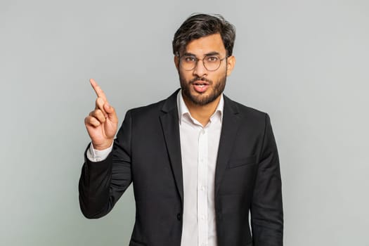 Indian businessman shakes finger and saying no, be careful, scolding giving advice to avoid danger mistake, disapproval sign, disagree, dislike. Arabian man in formal suit isolated on gray background
