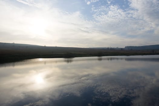 Horizontal wide angle image of a bright winters sky reflected in a calm reservoir. Redmires upper reservoir shown here very still and flat calm.