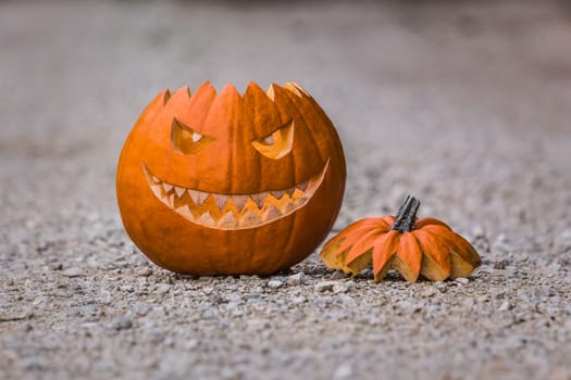 Big scary smiling halloween pumpkin with fiendish smile sitting on the floor outdoor. Spooky nightmare mystery scene at ocober 31st.