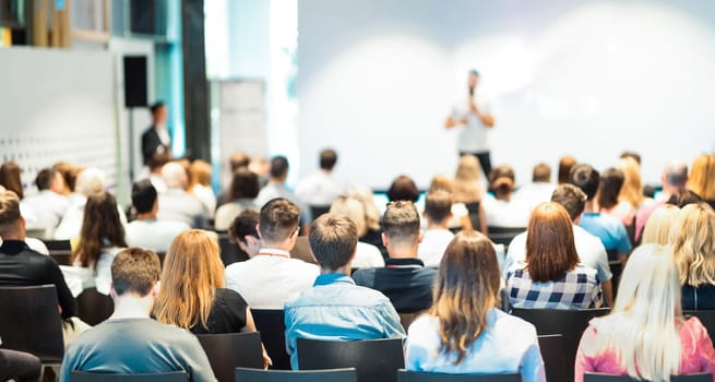 Speaker giving a talk in conference hall at business event. Rear view of unrecognizable people in audience at the conference hall. Business and entrepreneurship concept.