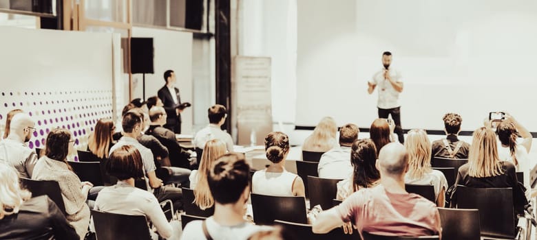 Speaker giving a talk in conference hall at business event. Rear view of unrecognizable people in audience at the conference hall. Business and entrepreneurship concept.