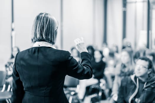 Female speaker giving a talk on corporate business conference. Unrecognizable people in audience at conference hall. Business and Entrepreneurship event.