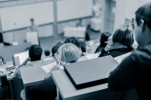 Speaker giving presentation in lecture hall at university. Participants listening to lecture and making notes