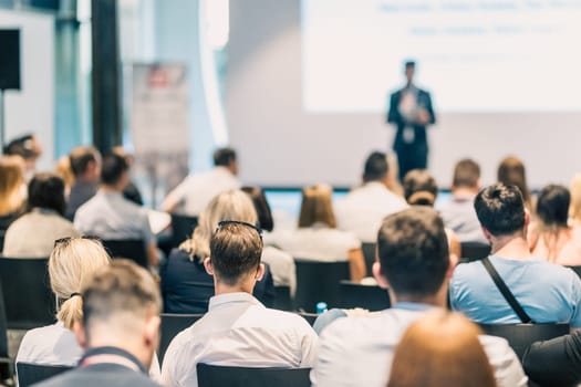 Speaker giving a talk in conference hall at business event. Rear view of unrecognizable people in audience at the conference hall. Business and entrepreneurship concept.