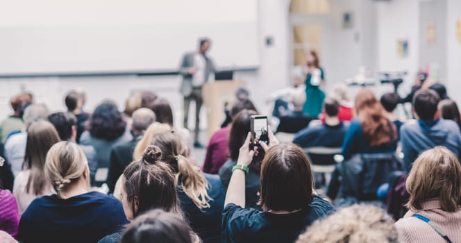 Male speaker giving presentation in lecture hall at university workshop. Audience in conference hall. Rear view of unrecognized participant in audience. Scientific conference event.