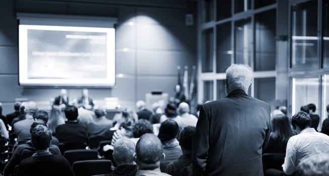 I have a question. Group of business people sitting at the chairs in conference hall. Businessman raising his arm. Conference and Presentation. Business and Entrepreneurship.