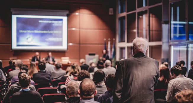 I have a question. Group of business people sitting at the chairs in conference hall. Businessman raising his arm. Conference and Presentation. Business and Entrepreneurship.