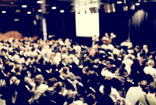 Business and entrepreneurship symposium. Speaker giving a talk at business meeting. Audience in conference hall. Rear view of unrecognized participant in audience.