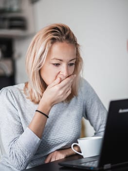 Female freelancer in her casual home clothing working remotly from her dining table in the morning. Home kitchen in the background