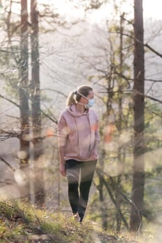 Portrait of caucasian sporty woman wearing a medical protection face mask while walking in the forest. Corona virus, or Covid-19, is spreading all over the world.
