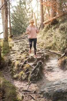 Active sporty woman listening to the music while running in autumn fall forest. Female runner training outdoor. Healthy lifestyle image of young caucasian woman jogging outside.