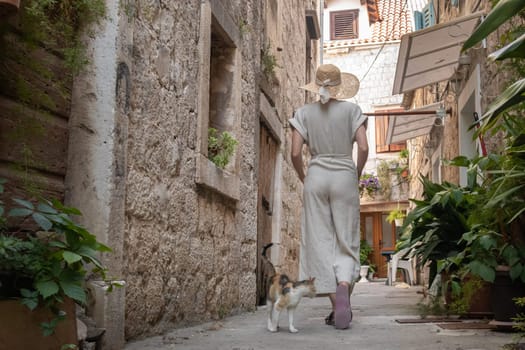 Rear view of beautiful blonde young female traveler wearing straw sun hat sightseeing and enjoying summer vacation in an old traditional costal town at Adriatic cost, Croatia.