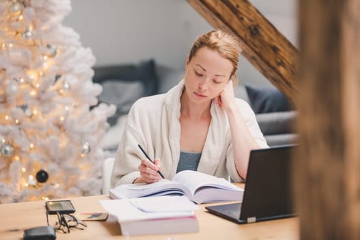 Young businesswoman wearing cosy warm bathrobe working remotly from home in winter Christmas time during 2020 corona virus pandemic. Work from home, selter in place, concept.