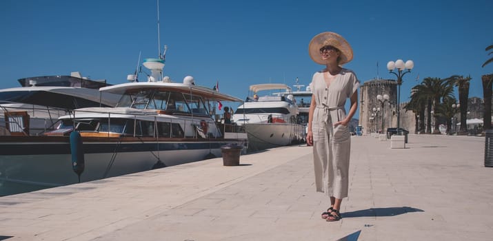 Young woman at the pier with sailing yachts. A beautiful girl walks near the moored sport yachts on a hot sunny summer day.