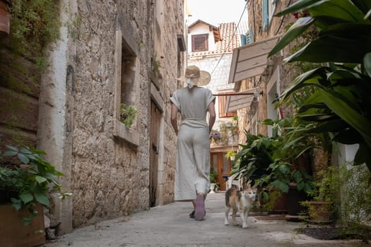 Rear view of beautiful blonde young female traveler wearing straw sun hat sightseeing and enjoying summer vacation in an old traditional costal town at Adriatic cost, Croatia.