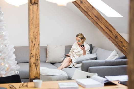 Young businesswoman wearing cosy warm bathrobe working remotly from home in winter Christmas time during 2020 corona virus pandemic. Work from home, selter in place, concept.