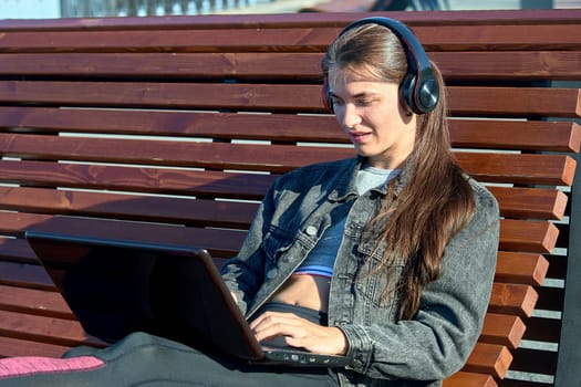 A woman with a laptop sits on an outdoor bench and works online. High quality photo