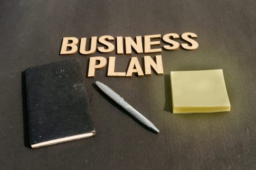 Businessman hand placing a pen and notebook in front of Word Business Plan made of wooden blocks of Alphabet letters. High Angle View. Vertical background. Close up
