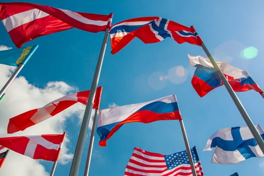 Bright flags of different countries against the blue sky and clouds