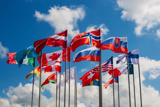 Bright flags of different countries against the blue sky and clouds