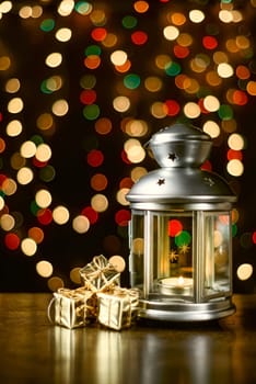 Christmas composition: a lantern with candles, bright shiny boxes with gifts, blurred bokeh lights in the background.