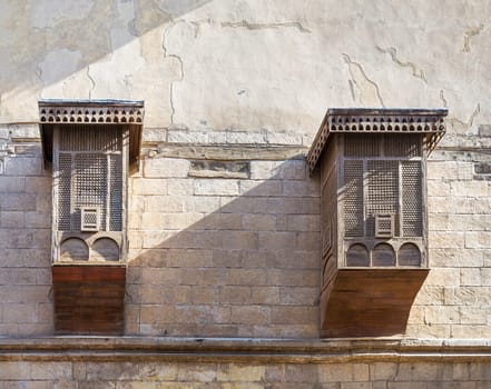 Two Mamluk era style oriel windows covered by interleaved wooden grid - Mashrabiya, on shabby grunge external wall, old Cairo, Egypt