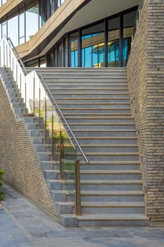 Stone staircase and railing leading to entrance of contemporary city office building with glass mirrored walls
