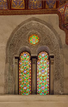 Two adjacent perforated stucco arched windows decorated with colorful stain glass with geometrical and floral patterns, at Mamluk era public historical Qalawun complex, Moez Street, Cairo, Egypt
