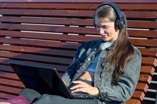 A woman with a laptop sits on an outdoor bench and works online. High quality photo