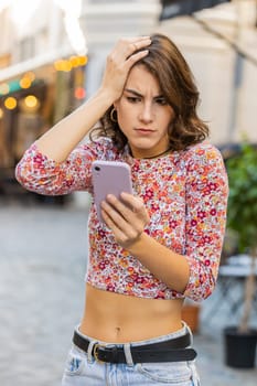Young woman use smartphone typing browsing, loses becoming surprised sudden lottery results, bad news, fortune loss, fail. Girl walking in urban city sunny street outdoors. Town lifestyles. Vertical