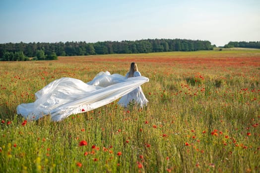 young woman with foil in poppy field, rear view