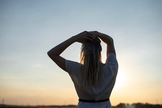 happy young blond woman enjoying sunset, rear view