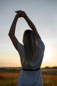 happy young blond woman enjoying sunset in poppy field