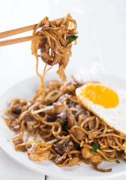 Close-up stir fried char kuey teow on chopstick over wooden background.