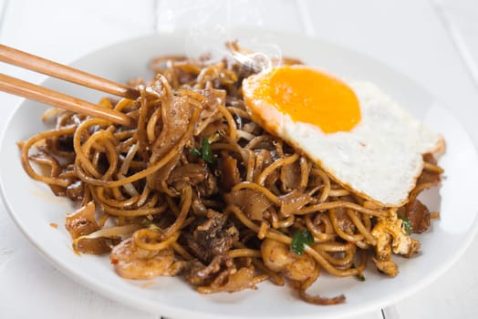 Close-up stir fried char kuey teow with chopstick over wooden background.