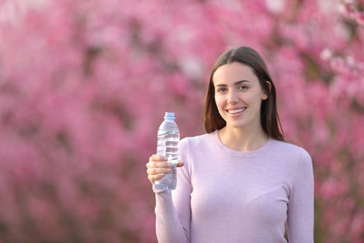Happy woman holding water bottle in a field looking at camera