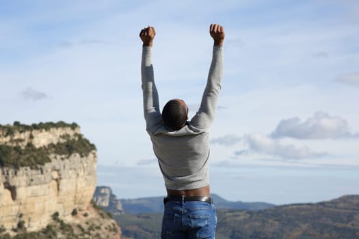 Back view portrait of an excited man with black skin raising arms in nature