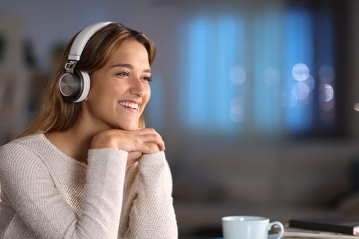Happy woman wearing headphones smiling listening to music at home in the night