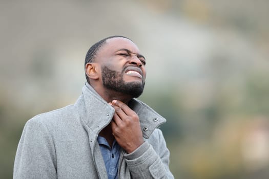 Sick man with black skin suffering sore throat outdoors in winter