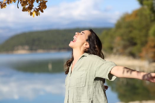 Side view portrait of a happy woman outstretching arms in a mountain lake